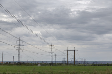 high-voltage power transmission lines in a green flat field against a cloudy sky.