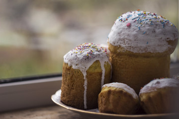 Easter cake with white icing and sprinkled with little candies on the plate on the window sill. A lot of cakes