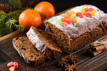 Freshly backed fruit cake with raisins, prunes and dried apricots decorated with candied fruits on dark oak board