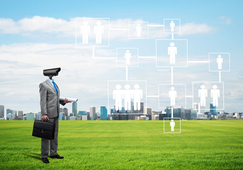 Camera headed man standing on green grass against modern cityscape