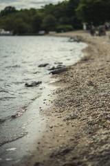 A close shot of water on a lake shore, with details of bubbles and little stones on the sand