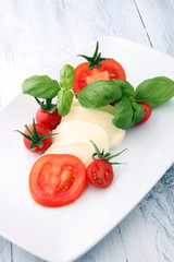 Obraz na płótnie Canvas Mozzarella and tomato with basil leaves on a white wooden background