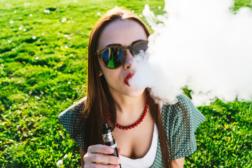 Happy fashion smiling Woman in sunglasses smoking vape on street,smoke