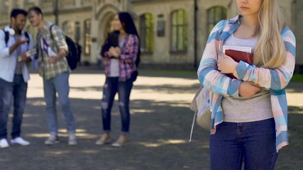 Students laughing and pointing to lonely sad girl standing aside, cruel bulling