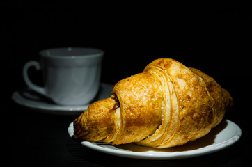 croissants on plate and cup of tea or coffee on dark wooden background