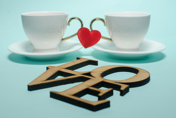Two white cups and a red heart on Valentine's Day stand on a turquoise background. Valentine's day card