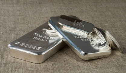Silver bullion (bars and coins) on a background of a rough wooden texture. .