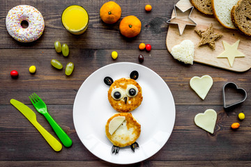Funny breakfast for children. Meal with cheesecake in shape of owl. Dark wooden background top view