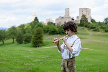 A boy in traditional Bavarian clothes with a shepherd's pipe on the background of ancient ruins.