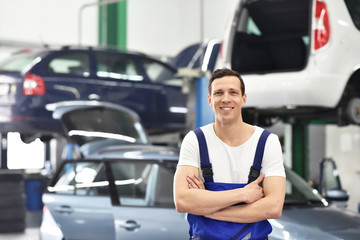 Portrait freundlicher KFZ Mechaniker in einer Autowerkstatt - im Hintergrund Fahrzeuge zur...