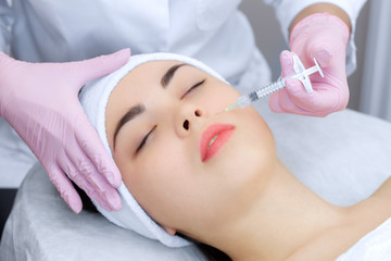 Naklejka premium The doctor cosmetologist makes the Rejuvenating facial injections procedure for tightening and smoothing wrinkles on the face skin of a beautiful, young woman in a beauty salon.Cosmetology skin care.