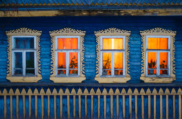 Bright yellow lighting carved windows of rural log house in the village