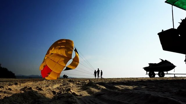 Silhouettes of people on the beach. They inflate and lift the parachute into the air. Water sports on the beach.