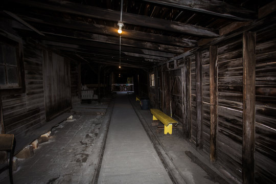 Bare wood walls and rafters in a long hallway with lit light bulbs hanging from beams in ceiling of an abandoned brick factory