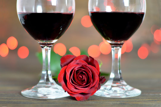 Valentines Day composition with two red wine glasses and red rose on wooden background.  Romantic celebration concept. 