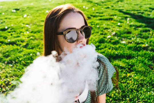 Happy fashion smiling Woman in sunglasses smoking vape on street,smoke