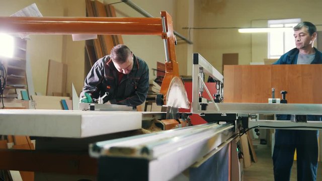 Workers carpenters are cutting wooden detail on electric saw at furniture factory