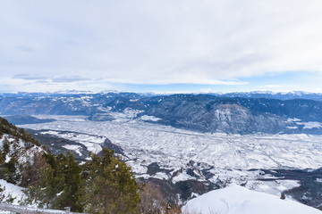 Snowy Adige valley seen from above. View of landscape of the alpine city between mountains, South Tyrol, Trentino. Aerial view of a valley during winter. Valley full of snow