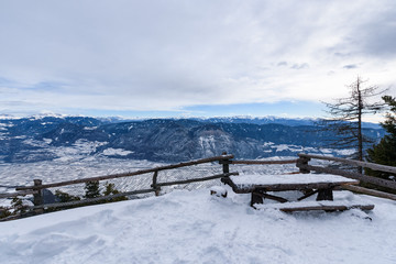Snowy Adige valley seen from above. View of landscape of the alpine city between mountains, South Tyrol, Trentino. Aerial view of a valley.Valley full of snow. A bench and a table in the foregound