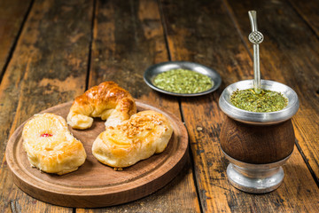 Traditional Argentinian yerba mate tea in a calabash gourd with bombilla stick and argentine pastries desserts against wooden background