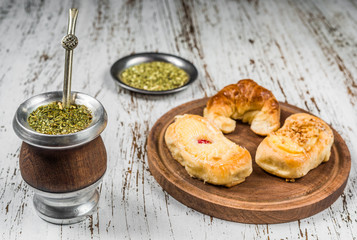Traditional Argentinian yerba mate tea in a calabash gourd with bombilla stick and argentine pastries desserts against wooden background