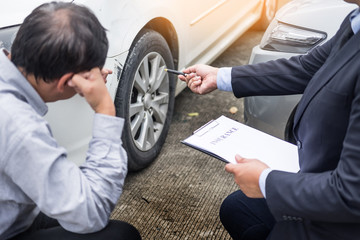 Insurance agent writing on clipboard while examining car after accident claim being assessed and...
