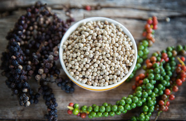 Ingredient white pepper on cup with branch of black pepper and fresh pepper.