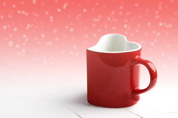 Red mug in shape of heart on white table at light red background with bokeh , front view. Valentine day concept background