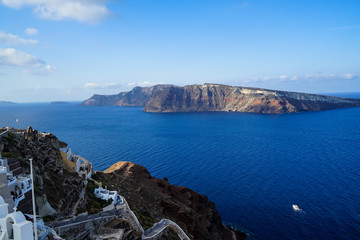 Beautiful view of vast blue Aegean sea, sailing ships and natural caldera mountain from Oia village with white buildings along island with blue sky background
