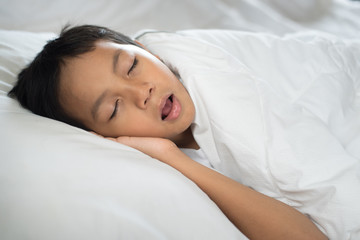 Obraz na płótnie Canvas young boy sleeping with mouth open (snoring) on bed white pillow and sheet.boy asleep and snoring.sleep concept