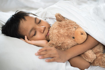 boy sleeping on bed with teddy bear white pillow and sheets.boy fall asleep in morning.sleep concept