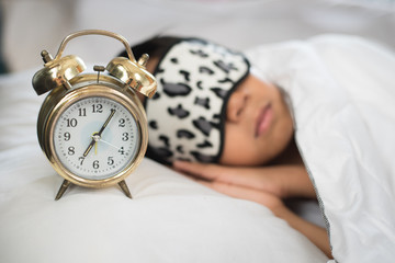 boy sleeping on bed white piilow and sheets with alarm clork wearing sleep mask.sleep concept