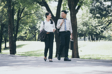 Happy Asian business man and woman walking and talking in the public park after finish work.