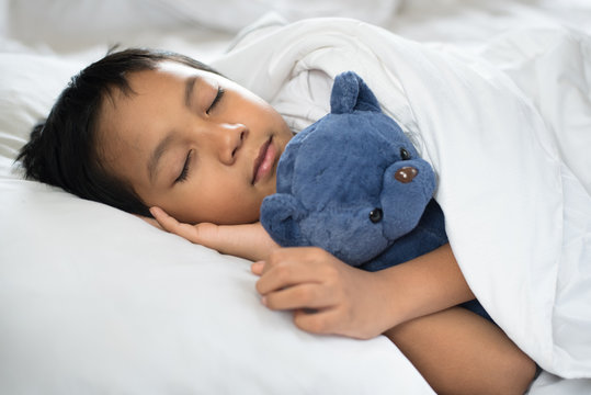 boy sleeping on bed with teddy bear white pillow and sheets.boy fall asleep in morning.sleep concept