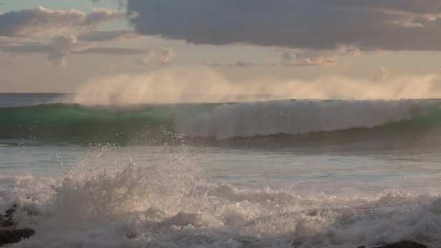 Shorebreak ocean waves near rocky coast and cliffs, rough sea water at sunset time