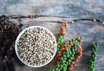 Ingredient white pepper on cup with branch of black pepper and fresh pepper.