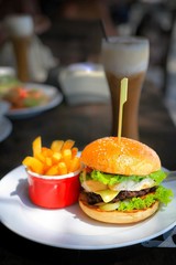 Shallow depth of field of Burger set on white plate with ice coffee on wood table.