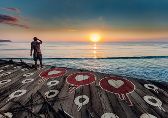 Surfer looking at the waves from old wooden pier at sunset in Bali