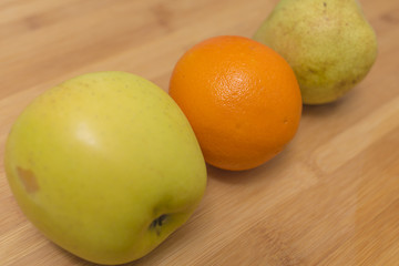 Three different fresh fruits apple orange and pear close up detail on a wooden table