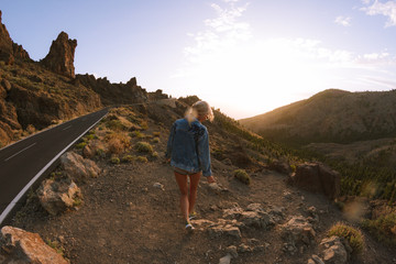 Girl in mini shorts and jeans jacket hiking and looking at sunset in desert nature