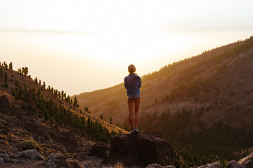 Girl in mini shorts and jeans jacket hiking and looking at sunset in desert nature