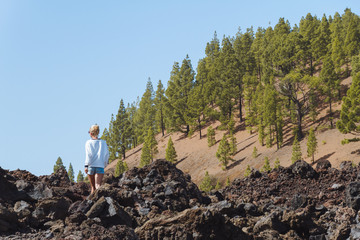 Girl walking in dark volcanic landscape with green trees