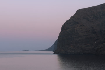 Fototapeta na wymiar Calm ocean water and big cliffs in dusk before sunrise