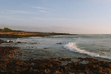 Surfers on ocean waves breaking on shore at dawn