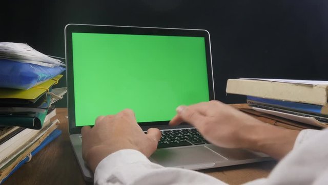 Close up of man works at laptop late ot office with Green Screen. Businessman working at night at the computer with Choma Key.
