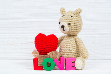 Sweet teddy bear doll  with Love text and red knitting heart on white wooden background and copy space for add text and picture, love and valentine day concept.