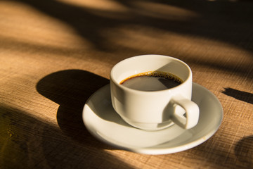 Hot black coffee on wood table in morning sunrise