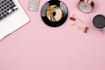 Flat lay home office desk workspace with laptop, coffee and donut, paperclip and calculator on pink background. Top view.