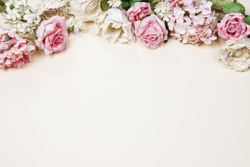 Frame made of pink and beige roses, green leaves, branches on beige background. Flat lay, top view. Wedding's background with copy space.