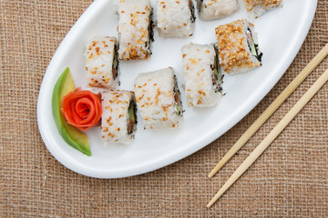 Uramaki sushi rolls with avocado and red fish on ceramic plate and wooden sticks